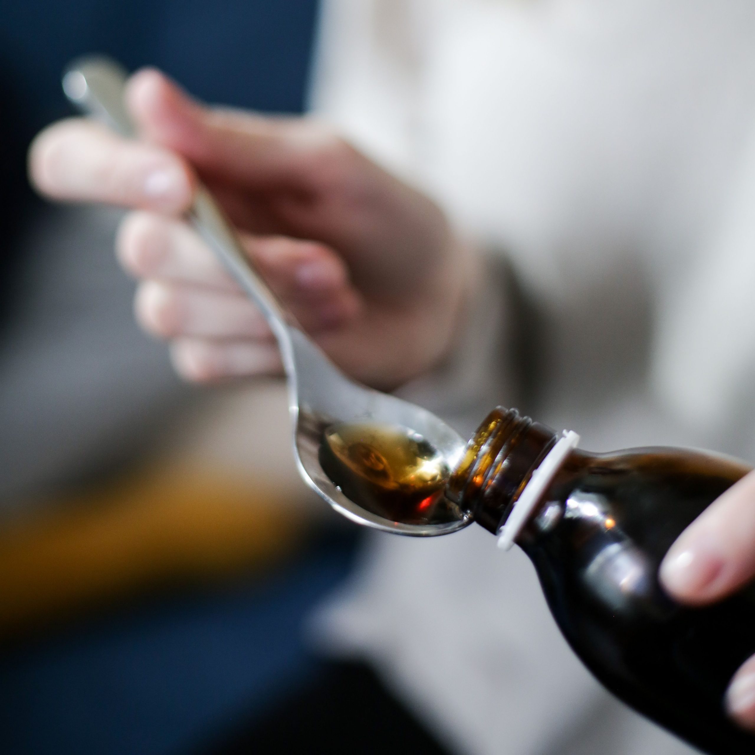Close-up of hand pouring cough syrup into a spoon, perfect for healthcare concepts.